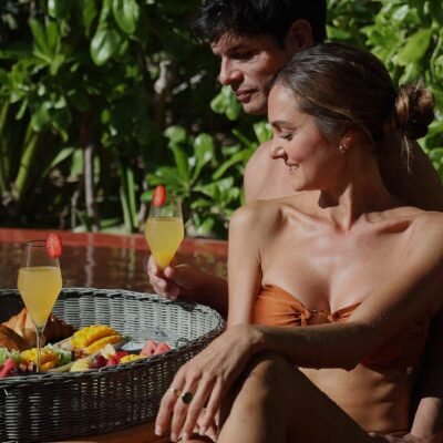 Pareja joven relajándose en la piscina con bebidas tropicales en un resort de lujo bajo el sol
